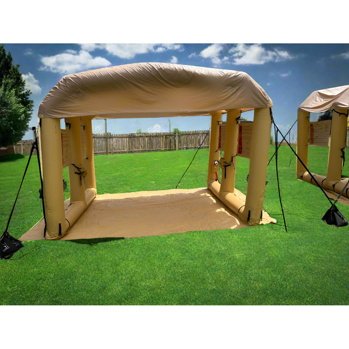 Tan inflatable LAMS L-10 air shelter with arched roof and open sides set up on a grassy field.
