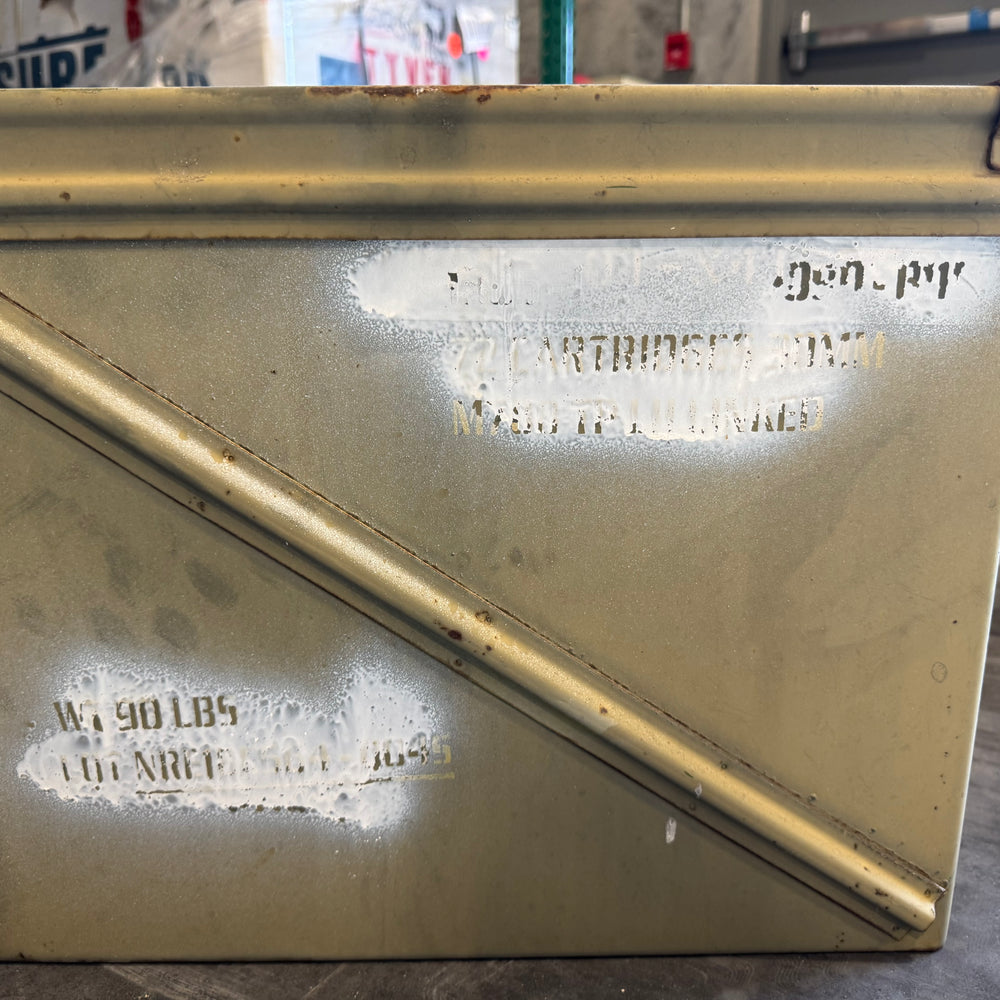 Yellow ammunition box with stenciled text on concrete floor, showing wear and markings.