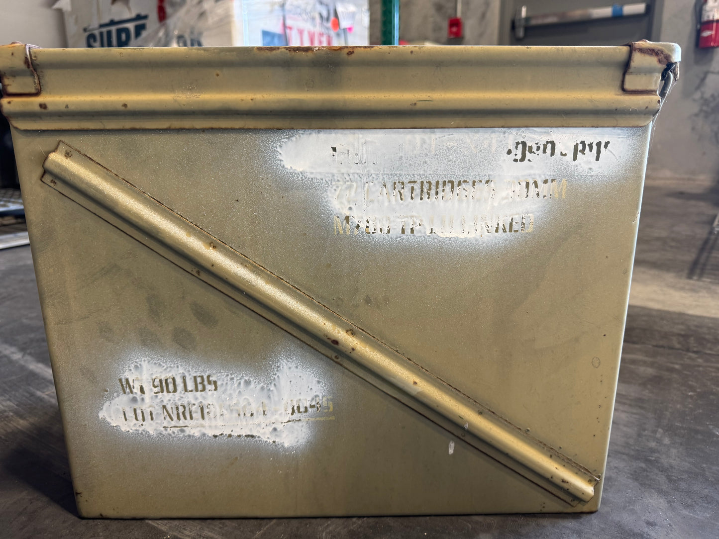Yellow ammunition box with stenciled text on concrete floor, showing wear and markings.